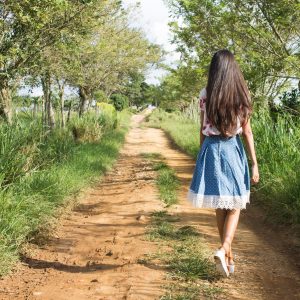 woman wearing blue and white skirt walking near green grass during daytime